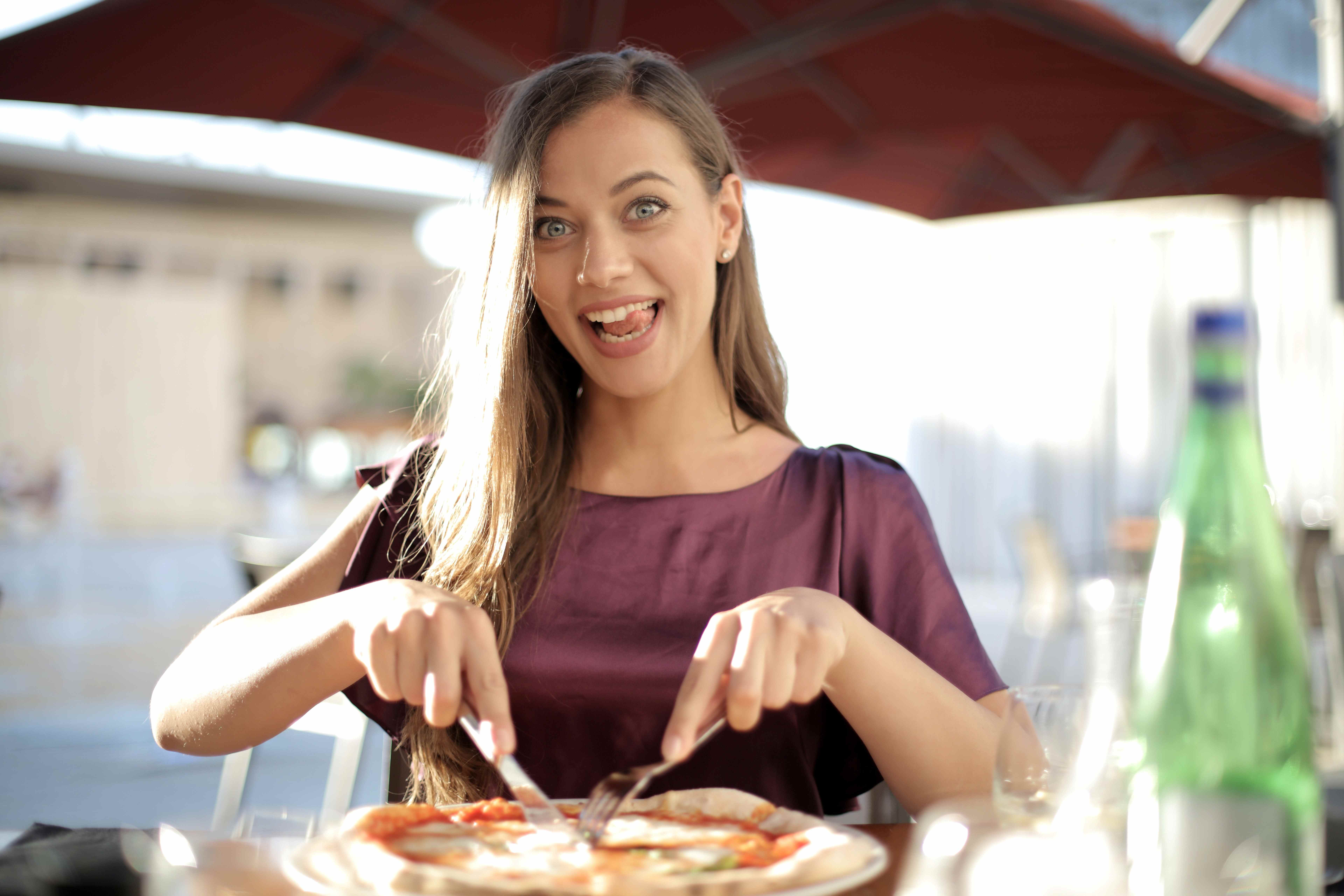 Žena jí ve venkovní restauraci pizzu u jídelního stolu.
